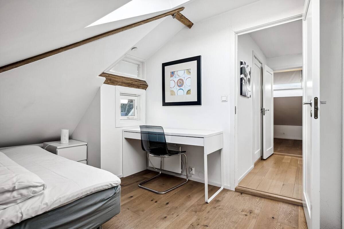 A bedroom with a sloped ceiling, a desk with a chair, a bed, and a wardrobe.