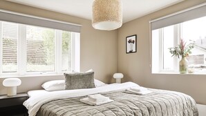 A bedroom with a large bed, bedside tables, a hanging light fixture, and a window with blinds. - Staysville – City Center (Stavanger)