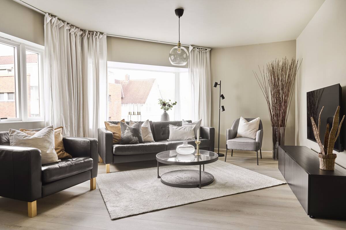 A modern living room with a sofa, armchair, coffee table, and a large window with curtains.
