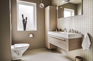 Een moderne badkamer met toilet, wastafel met spiegel en raam met een cactus.