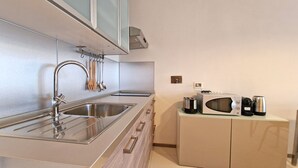 A modern kitchen with stainless steel appliances, a sink, and wooden utensils hanging on the wall. - Suite La Giudecca (Gallipoli)