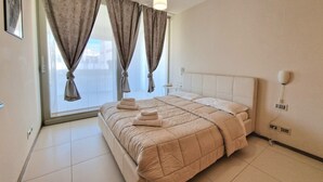 A bedroom with a bed, curtains, a bedside table, and a wall-mounted lamp. - Suite La Giudecca (Gallipoli)