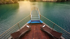 A boat deck with a view of a calm river and surrounding cliffs at sunset. - La Pandora Boutique Cruise (Tuan Chau)