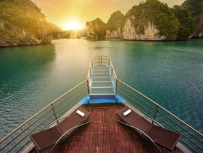 A boat deck with a view of a calm river and surrounding cliffs at sunset. - La Pandora Boutique Cruise (Ha Long)
