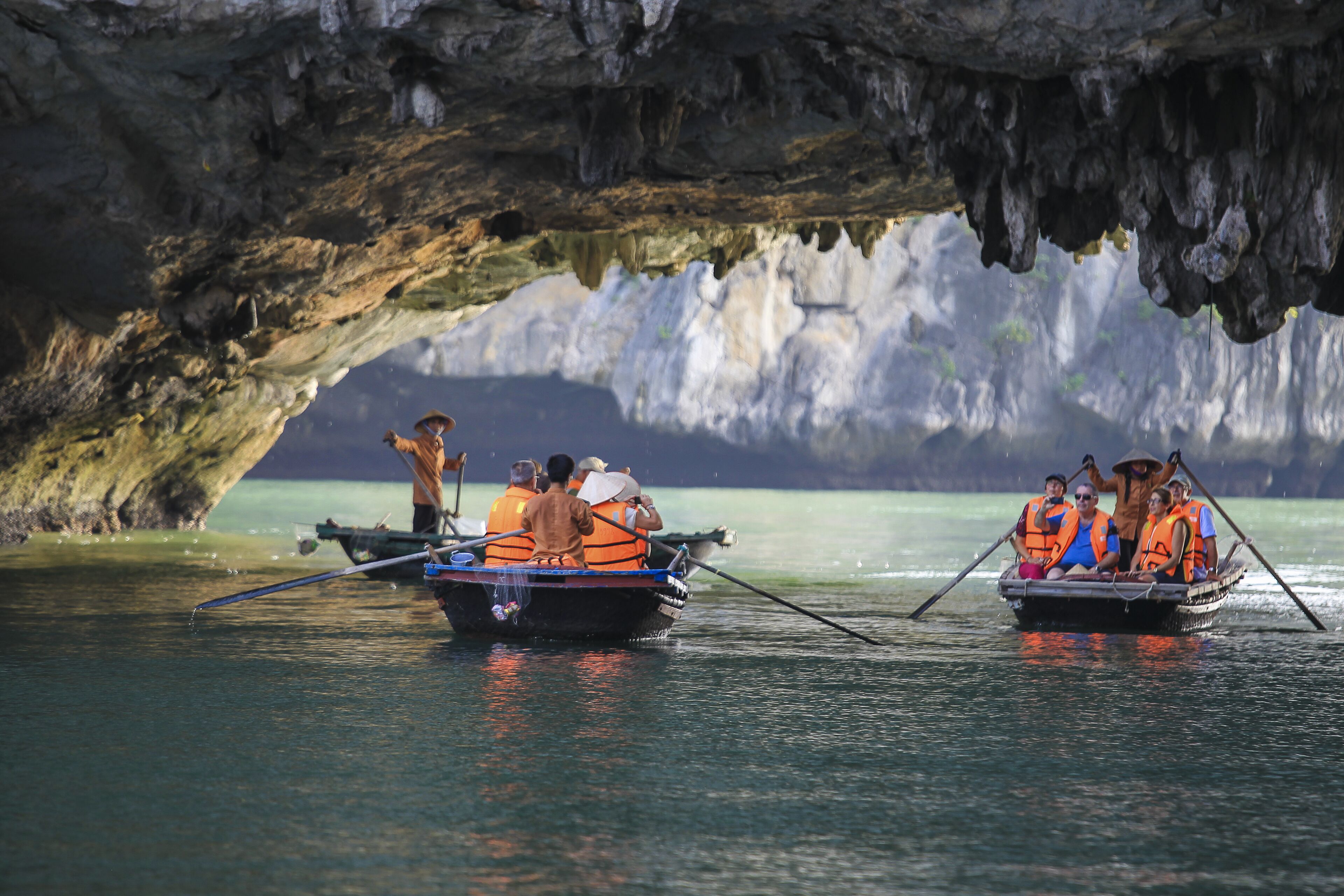 Deux bateaux transportant des passagers portant des gilets de sauvetage naviguent sur un cours d’eau, avec en arrière-plan une formation rocheuse ressemblant à une grotte.