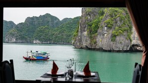A table with a view of a boat on water and a cliff. - La Pandora Boutique Cruise (Tuan Chau)