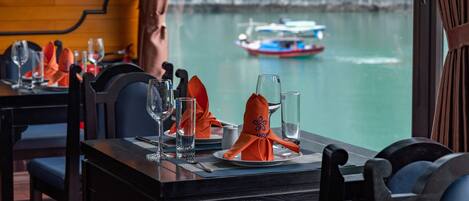 A dining table set with plates, glasses, and cutlery, overlooking a body of water with a boat.