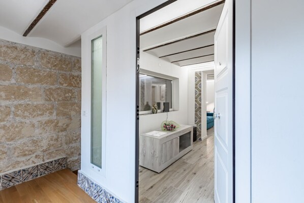 Un couloir avec un mur en pierre, un plancher en bois, un comptoir d’accueil avec un miroir et une porte donnant sur une autre pièce.