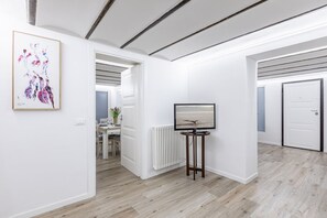 A modern interior with a white wall, a framed abstract painting, a round table with a flat-screen TV, and a wooden floor.