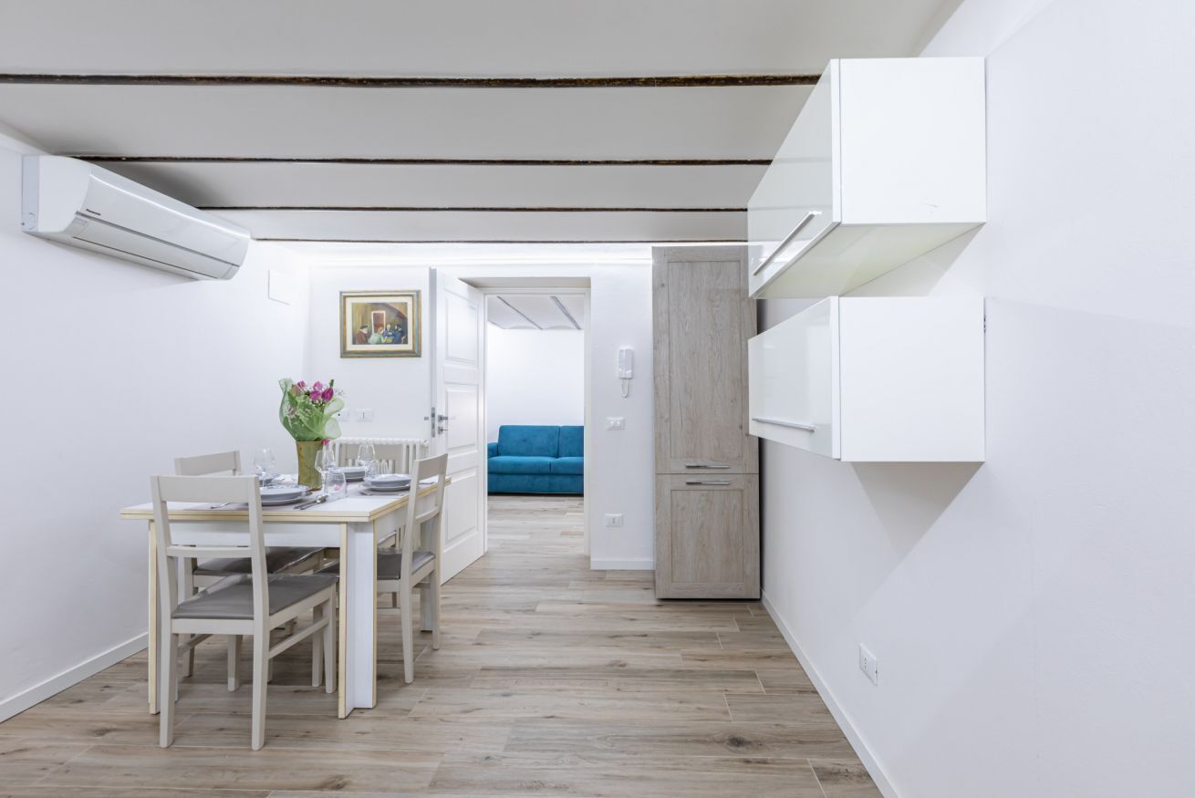 Un espacio habitable compacto con comedor, kitchenette y un sofá azul al fondo.