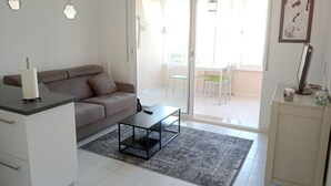 Een moderne woonkamer met een bank, een salontafel en een glazen schuifdeur die leidt naar een buitenruimte met stoelen.