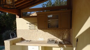A compact kitchen with a built-in oven, a sink, and a window overlooking a garden. - Bedroom and bathroom with summer kitchen, 12-minute walk to beach (Bormes-les-Mimosas)