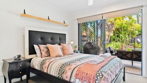 A bedroom with a large bed, a nightstand, a headboard, and a view of the outdoors through a sliding door.