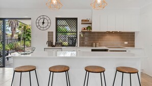 A modern kitchen with a white island, bar stools, a clock, and pendant lights.