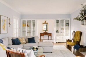 Una sala de estar con sofá, sillón y una mesa de centro. Se observan muebles con puertas de vidrio y un espejo en la pared.