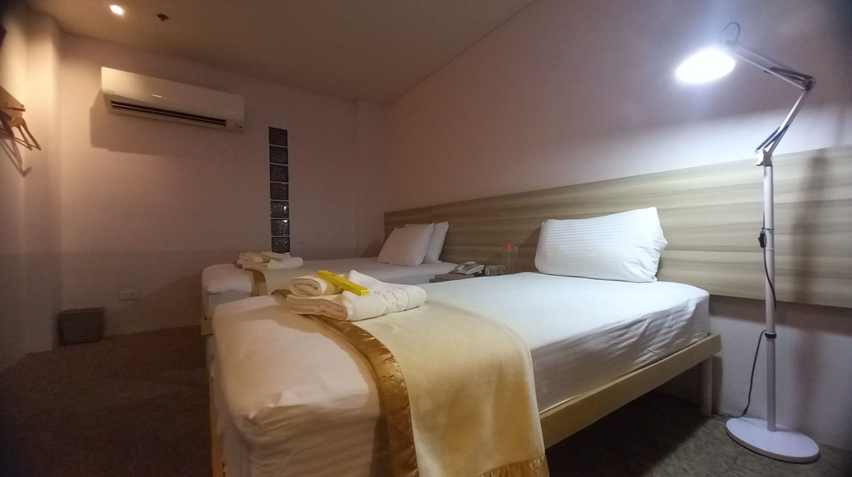 Een hotelkamer met een groot bed, een nachtkastje, een lamp en een airconditioner.