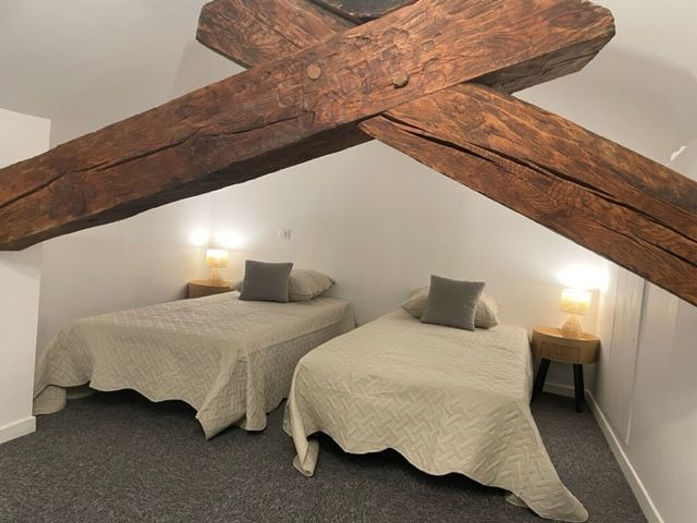 A bedroom with two beds, wooden beams, and bedside lamps.