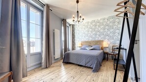 A bedroom with a wooden floor, a bed with a headboard, a hanging light fixture, and a window with curtains. - Comfortable lodging in Saugues for hikers, 3 spacious rooms with en-suite bathroom (Saugues)