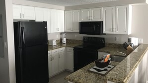 Una cocina moderna con armarios blancos, un refrigerador negro, un microondas, una estufa y una encimera de granito.