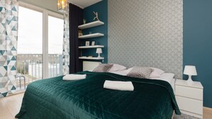 A modern bedroom with a large bed, a nightstand, a wall-mounted shelf with decorative items, and a view through a window. - Stylish Apartment in Wola | 450 m to the Metro, Balcony (Warszawa)