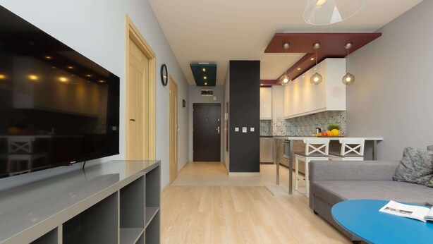 A modern living room with a flat-screen TV, a sofa, a coffee table, and a dining area with a table and chairs. - Stylish Apartment in Wola | 450 m to the Metro, Balcony (Warszawa)