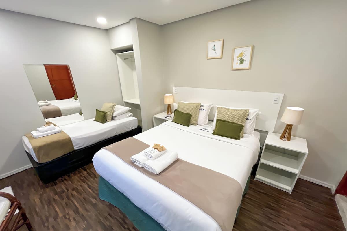 A hotel room with two beds, a large mirror, bedside tables with lamps, and a wooden floor.