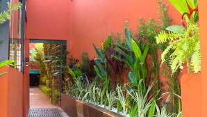 A narrow alleyway with a red wall, a metal gate, and various plants along the sides. - GoodStay São Paulo Ibirapuera (São Paulo)