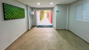 A hallway with a checkered wall art, a green exit sign, and a mat with 'GOOD STAY' text. - GoodStay São Paulo Ibirapuera (São Paulo)