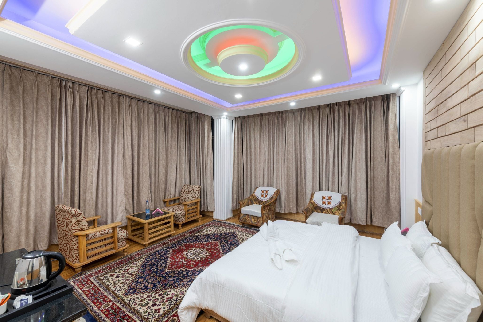 A hotel room with a bed, two armchairs, a small table, a decorative rug, and a ceiling with a circular light fixture.