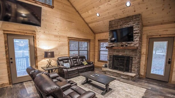 Interior acogedor de una cabaña de madera con chimenea de piedra, sofá de cuero y televisor de pantalla plana montado en la pared.