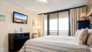 Une chambre d’hôtel dotée d’un grand lit, d’un téléviseur à écran plat fixé au mur, d’une commode, d’une lampe et offrant une vue sur l’extérieur grâce à une porte-fenêtre coulissante.