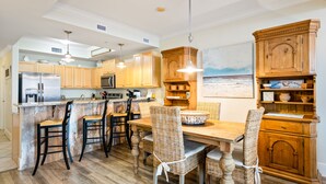 Une cuisine avec des meubles de rangement en bois, un îlot central doté de tabourets, et une table à manger avec des chaises.