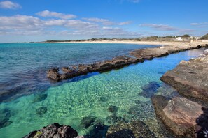 A coastal scene with clear turquoise water, rocky formations, and a sandy beach in the background. - 3157 Angolo di Paradiso by Barbarhouse (Porto Cesareo)