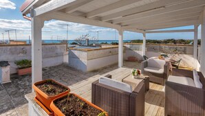Ein Terrassenbereich im Freien mit Korbmöbeln, Topfpflanzen und Meerblick.