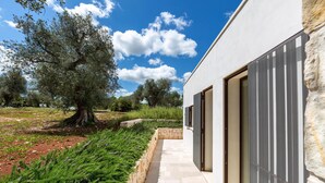 A modern building with a stone pathway leading to a door, surrounded by greenery and trees. - 3155 Villa Pietralunga by Perle di Puglia (Ostuni)