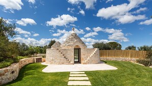A stone structure with a central door and two conical roofs, surrounded by a well-manicured lawn and stone walls. - 3155 Villa Pietralunga by Perle di Puglia (Ostuni)