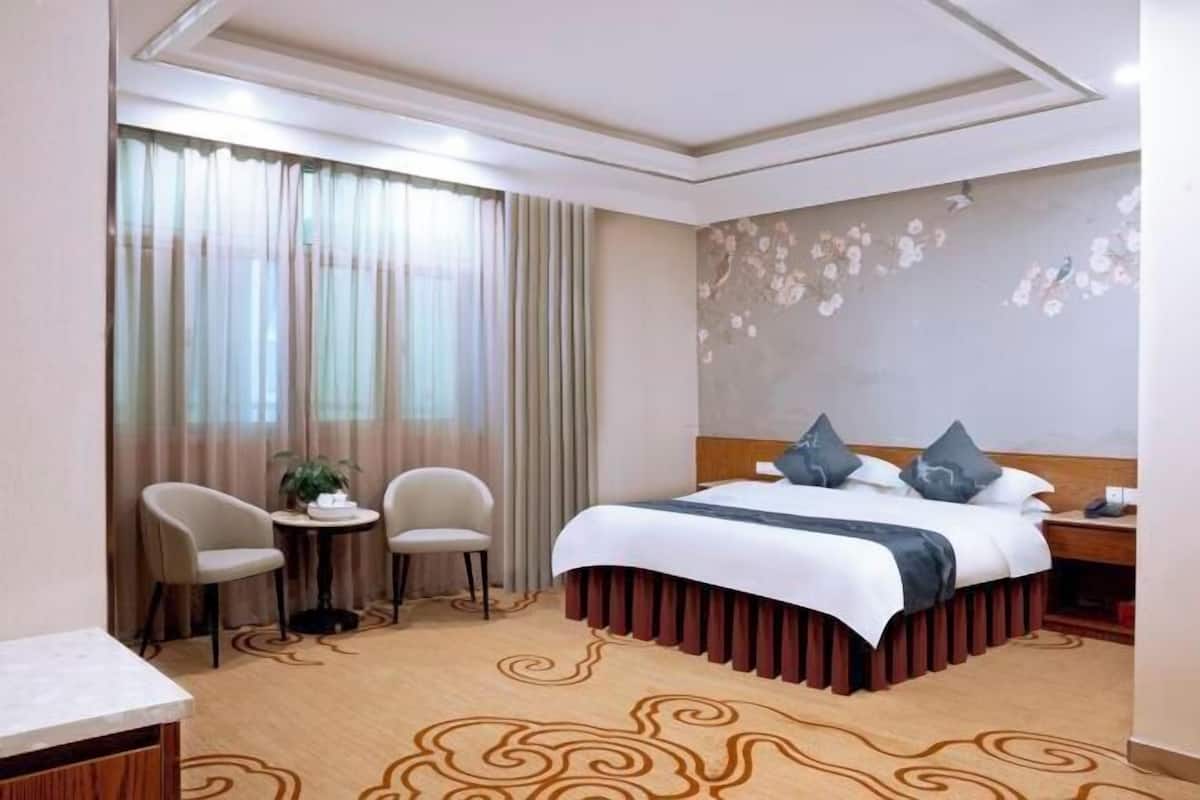 A hotel room with a bed, two chairs, a small table, and a nightstand.