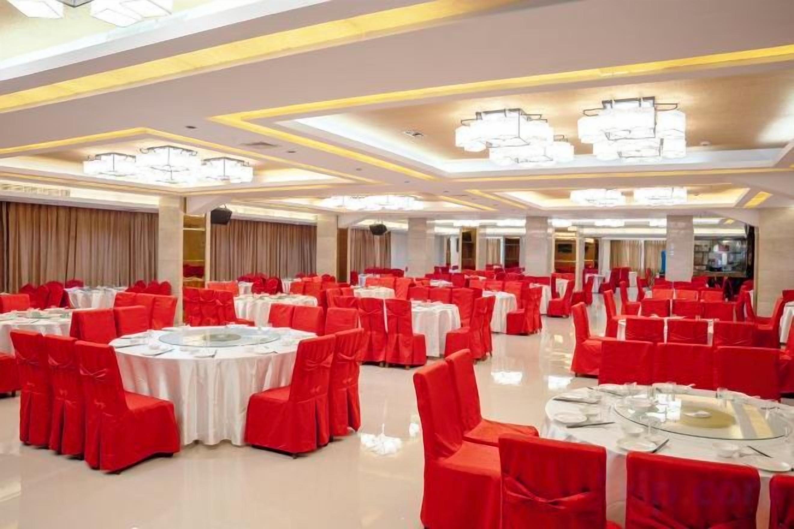 A banquet hall with round tables and red chairs, large chandeliers, and a polished floor.
