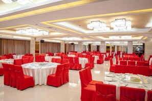 Un salón de banquetes con mesas redondas y sillas rojas, grandes candelabros y un suelo pulido.