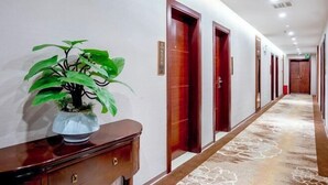 A hotel hallway with wooden doors, a potted plant, and a carpeted floor. - Zhongnan Hotel (Nan'an)