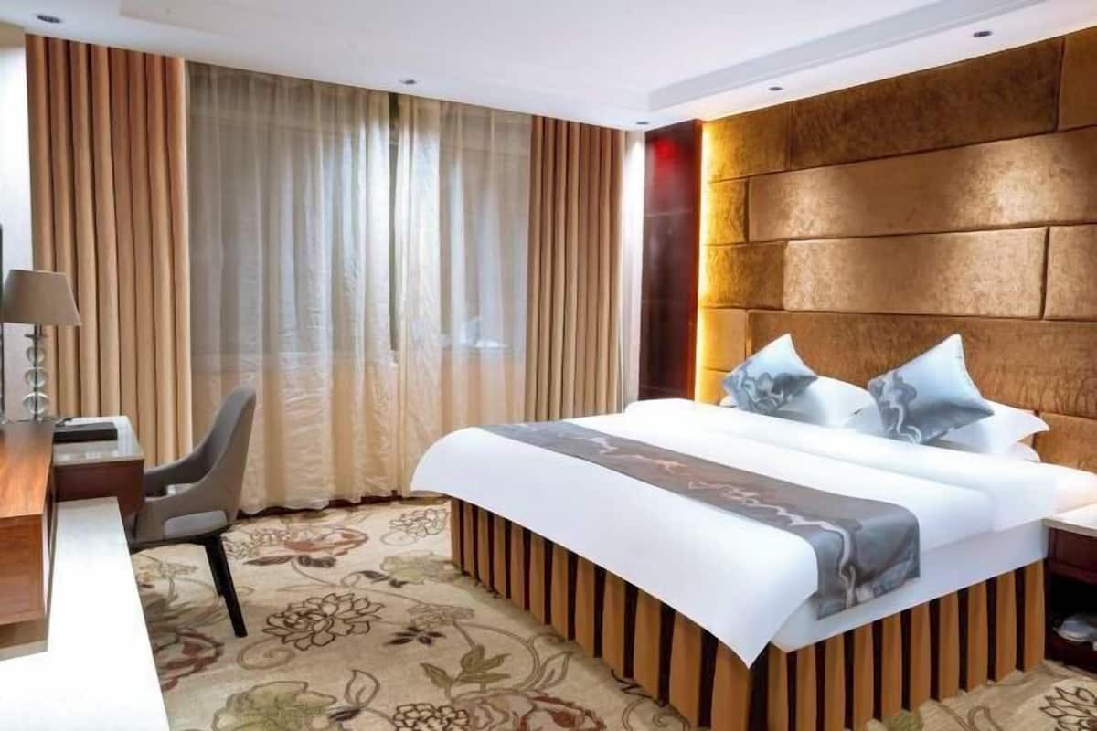 A hotel room with a large bed, a desk, a chair, and curtains.