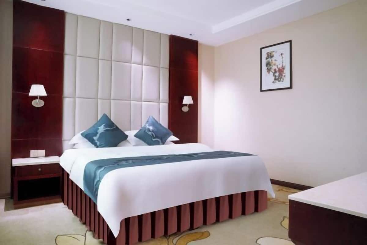 A hotel room with a large bed, two bedside tables, a nightstand, a desk, and a chair.