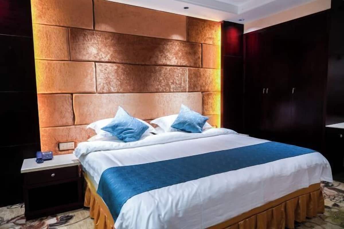A hotel room with a large bed, a nightstand, a wardrobe, and a textured wall.
