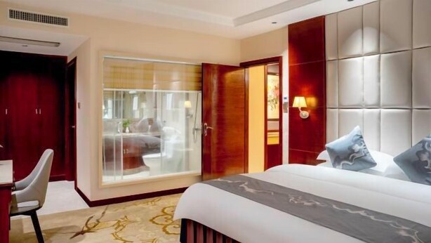 A hotel room with a bed, a desk, a chair, a sliding glass door, and a wall-mounted light fixture. - Zhongnan Hotel (Nan'an)