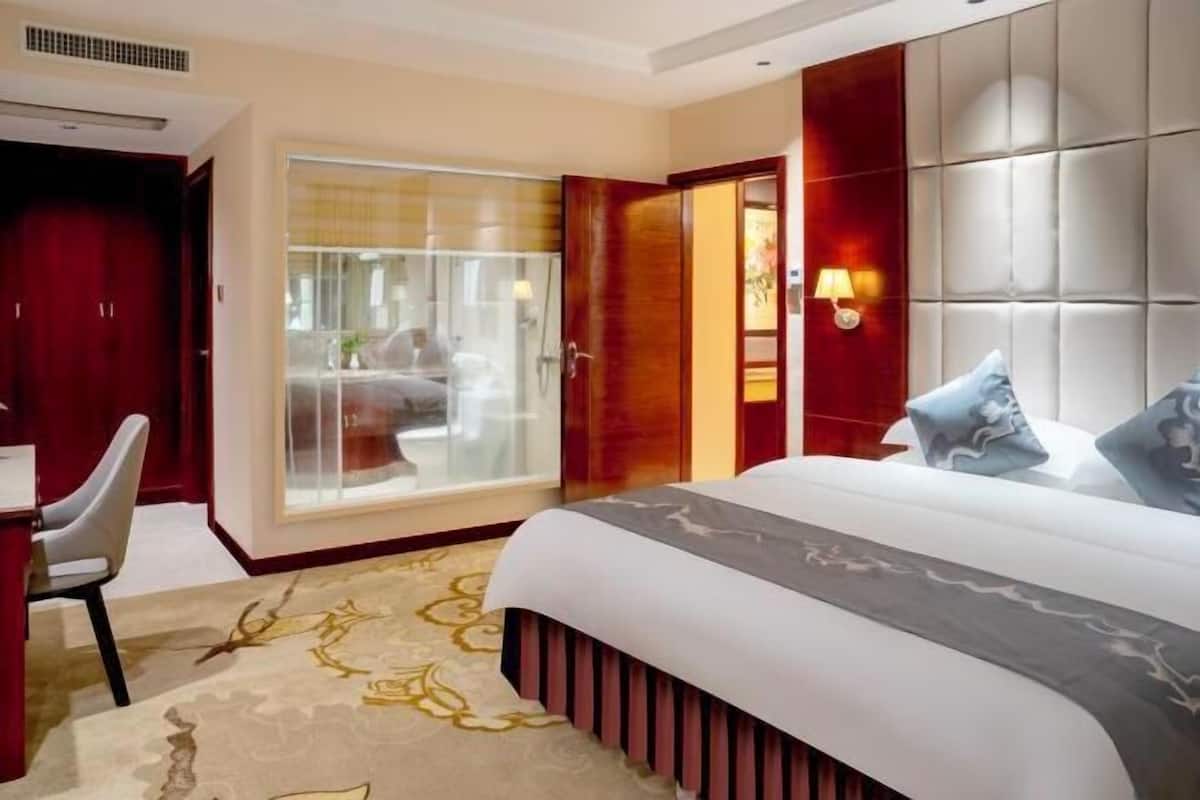 A hotel room with a bed, a desk, a chair, a sliding glass door, and a wall-mounted light fixture.