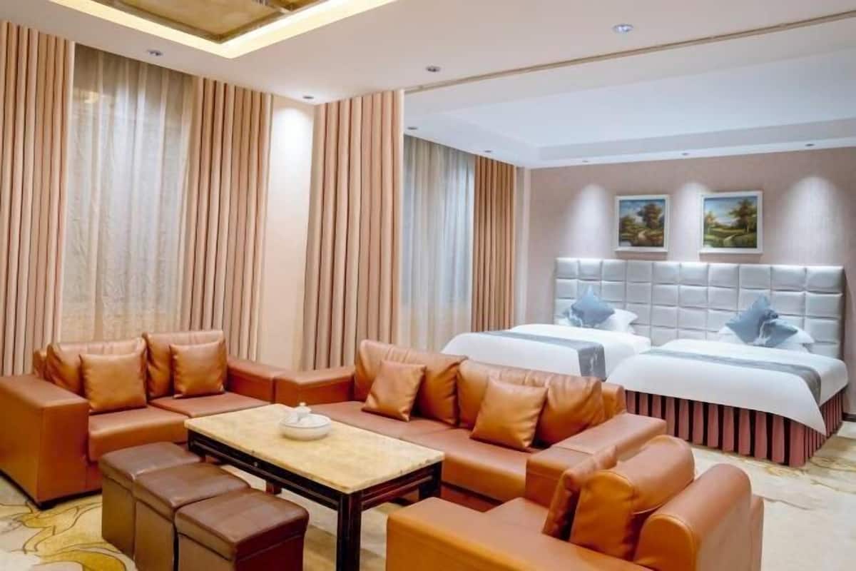 A hotel room with a sofa set, a bed, a small table, and two paintings on the wall.