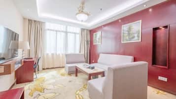 A hotel room with a red accent wall, a sofa, a coffee table, a TV, and a desk with a lamp.