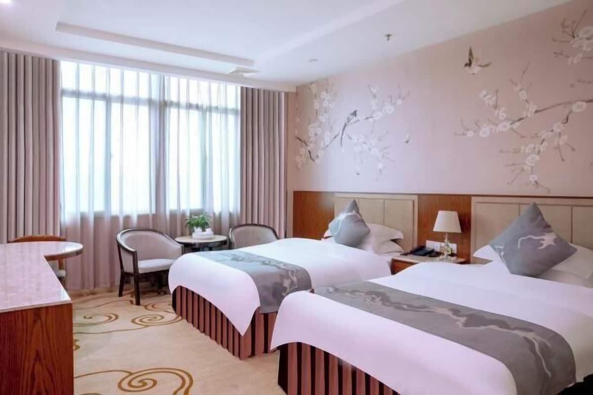 A hotel room with two beds, a desk, a chair, and a window with curtains.