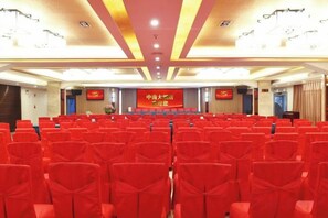 Un salón de conferencias con hileras de sillas, un escenario con un atril y un cartel.