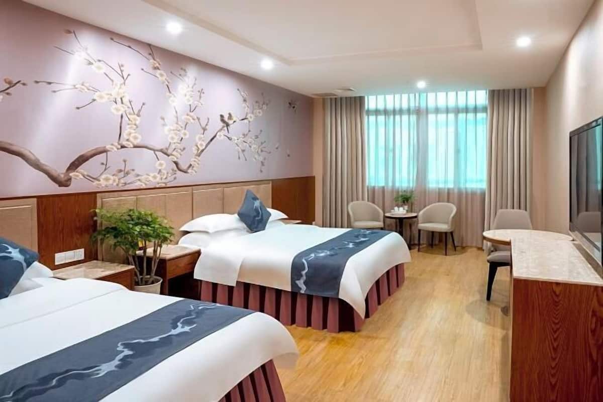 A hotel room with two beds, a desk, a chair, a TV, and a window with curtains.